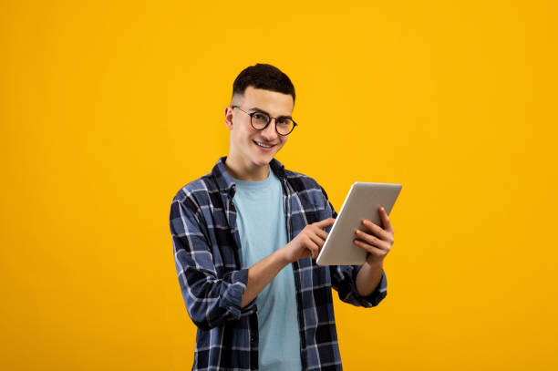 オンラインライフコンセプト。オレンジ色のスタジオの背景にタブレットpcを使用してファンキーな若者 - ipad people holding young adult ストックフォトと画像