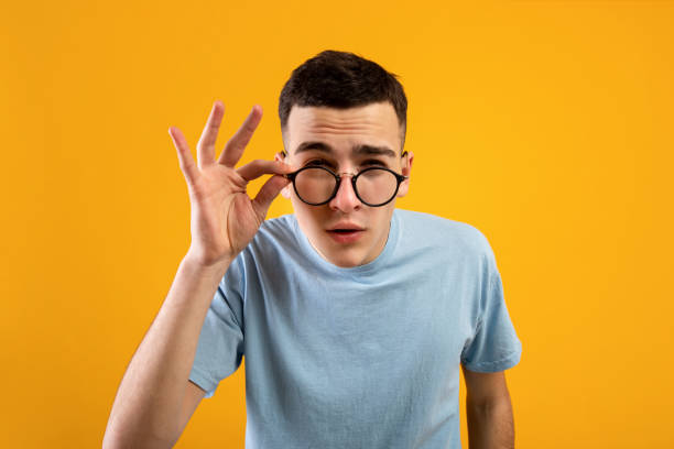 young caucasian man in glasses being skeptical, looking suspicious, having some doubt on orange studio background - eyes narrowed imagens e fotografias de stock