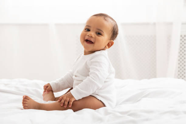 portret van afrikaanse baby peuter glimlachende zitting op bed indoor - lachen fotos stockfoto's en -beelden