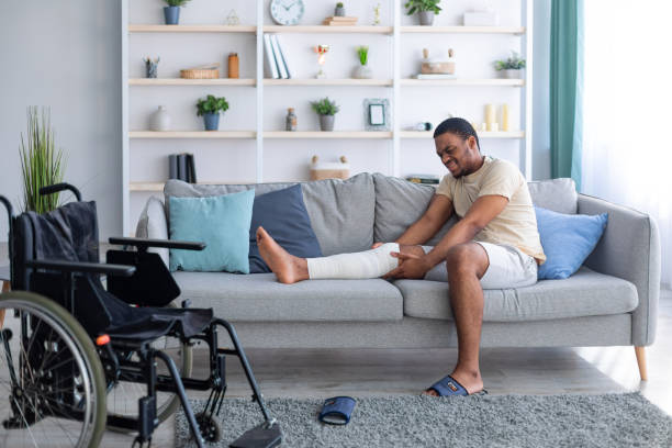 istock Millennial black man having plastered broken leg, suffering from pain on sofa at home, wheelchair standing nearby 1311428027