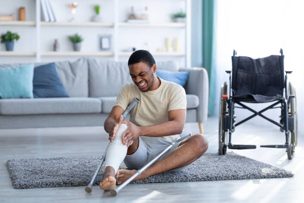 istock Young black man suffering from pain in plastered broken leg, sitting on floor after falling with crutches, indoors 1311428276
