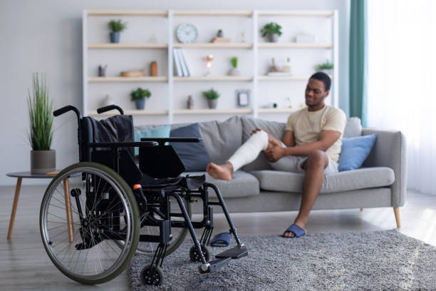 istock Young black guy with plastered broken leg sitting on sofa, focus on empty wheelchair, copy space 1311428782