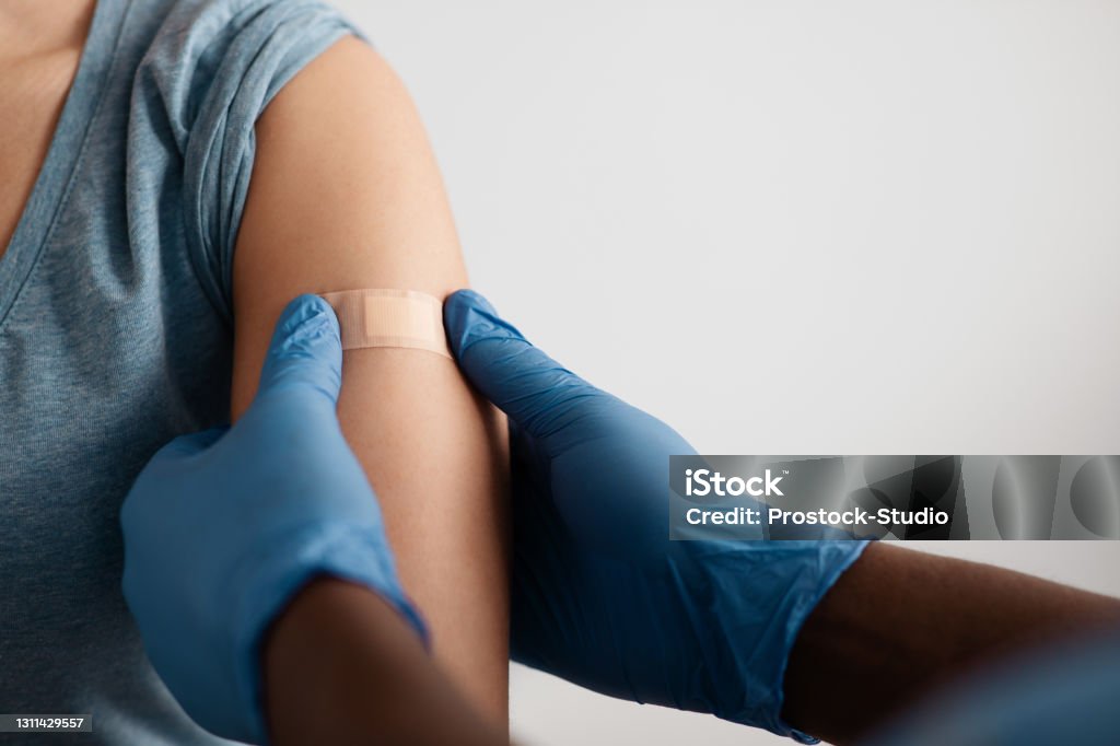 Vaccination of patients in hospital against covid-19 pandemic Vaccination of patients in hospital against covid-19 pandemic. Hands of african american doctor in protective gloves puts band aid to inculcate site to patient in clinic, close up, free space, cropped Vaccination Stock Photo