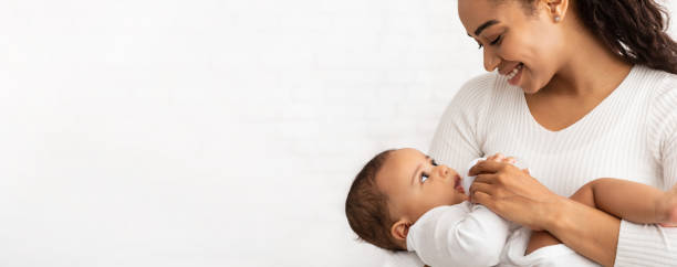 African Mother Feeding Baby Standing On White Background, Panorama, Cropped Happy African Mother Feeding Baby Giving Bottle With Milk To Her Newborn Son Standing Posing On White Studio Background. Infant's Nutrition And Child Care Concept. Panorama With Copy Space, Cropped breastfeeding photos stock pictures, royalty-free photos & images