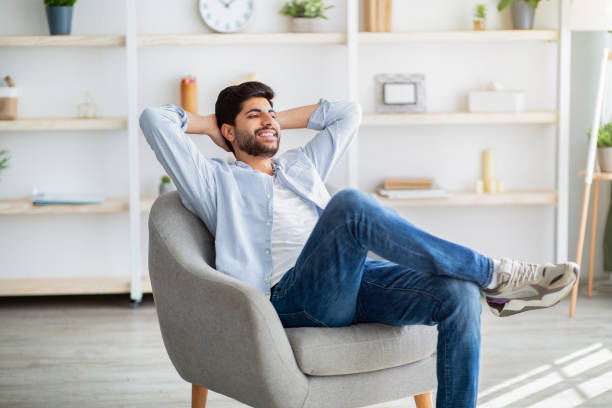 Lazy day. Relaxed arab man resting on comfortable armchair, holding hands behind head