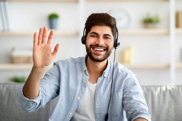istock Greeting concept. Arab man wearing headset and waving hand to camera, gesturing hello and smiling 1311431359