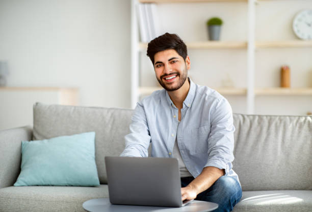 istock Successful remote freelancer working distantly at laptop computer and smiling to camera, sitting on couch 1311431969
