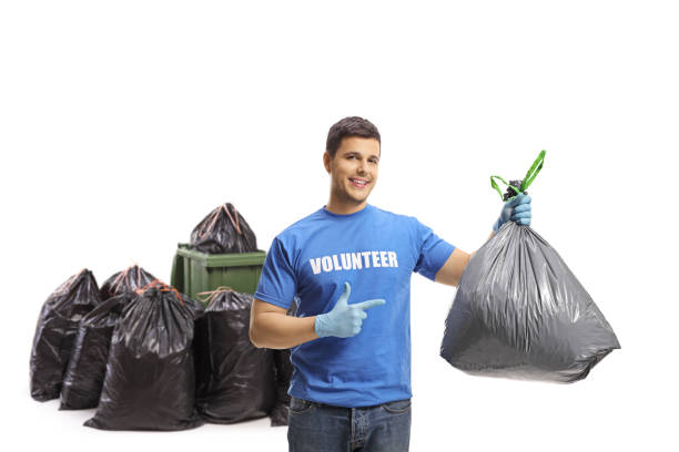 istock Young volunteer with a plastic garbage bag pointing at it in front of bins 1311432063