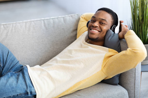 istock Black guy in wireless headset resting on couch at home 1311432235