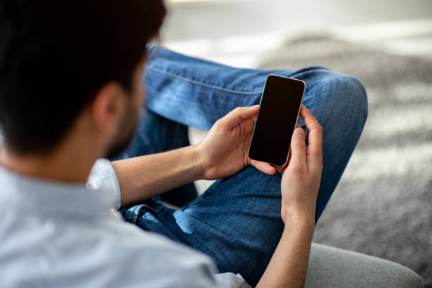 istock Over the shoulder view of unrecognizable man using cellphone with black empty screen for mockup 1311432309