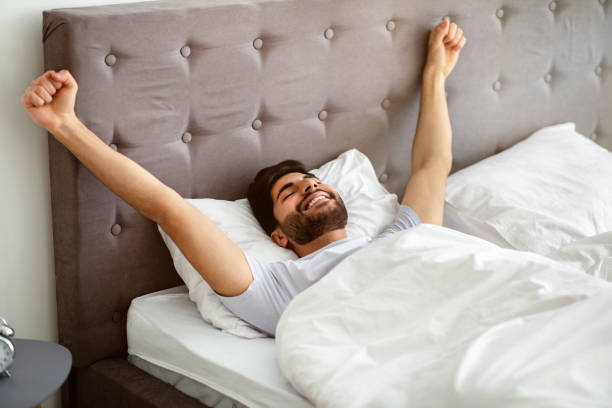 istock Wellslept arab guy waking up and stretching hands, lying in comfortable bed with eyes closed 1311432322