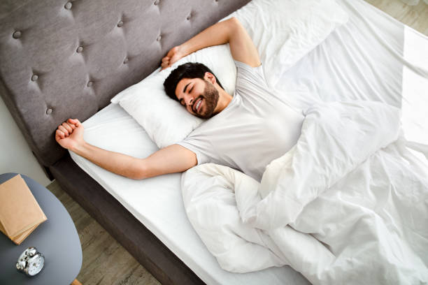 istock Comfortable sleep. Happy rested arab man waking up, stretching hands in bed and smiling with eyes closed. 1311432384