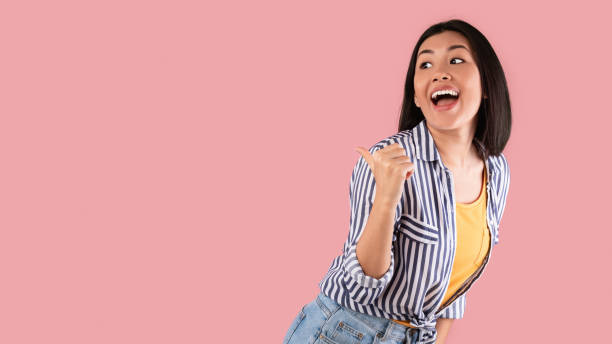 istock Smiling asian woman pointing thumb aside at copy space 1311433645