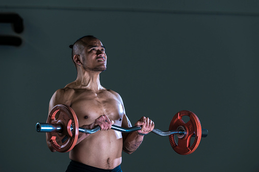 Muscular man working out in gym doing exercises with barbell at biceps