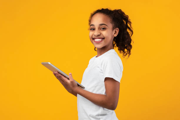 istock Black girl standing with tablet at yellow studio 1311433714
