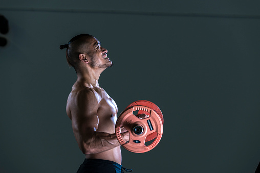 Muscular man working out in gym doing exercises with barbell at biceps