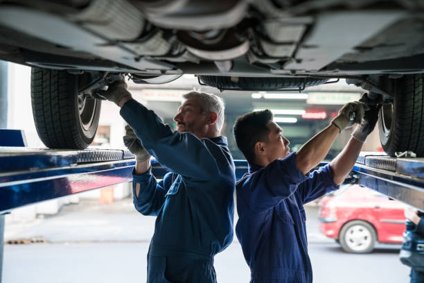 kfz-mechaniker überprüfen fahrzeugfahrwerk - maintenance engineer car lamp protective workwear stock-fotos und bilder
