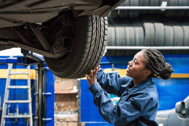 female car mechanic checking car wheel - trainee working car mechanic imagens e fotografias de stock