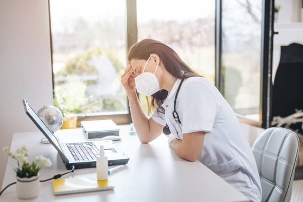 istock Tired doctor with face mask sitting at table in office 1311438265