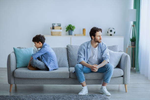 Annoyed father sitting back to back with son on sofa, ignoring each other after argue Family problems concept. Annoyed father sitting back to back with son on sofa, ignoring each other after argue. Stubborn dad and boy don't looking or speaking after conflict communication problems stock pictures, royalty-free photos & images