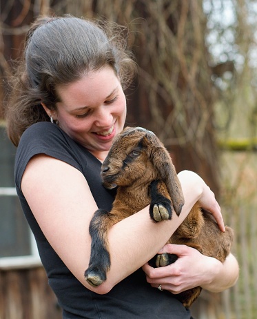 Young woman farmer with adorable baby goat in the arms (Capra aegagrus hircus)