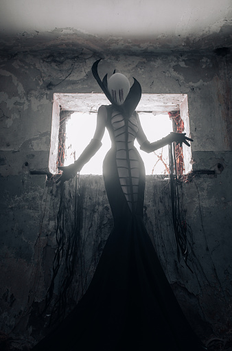 Woman in the image of the alien creature stands inside old abandoned house.