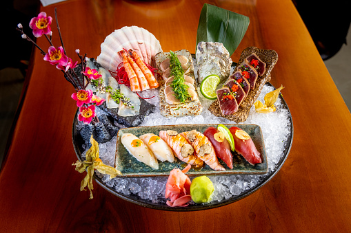 Japanese raw food delicacies in decorated serving dish full of ice, nigiri, tataki, prawn and tuna slices with ginger and wasabi