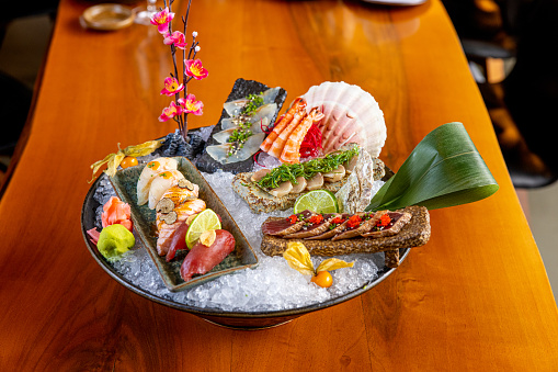 Japanese raw food delicacies in decorated serving dish full of ice on restaurant table, nigiri, tataki, prawn and tuna slices with ginger and wasabi