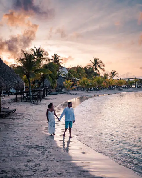 Tropical luxury resort Curacao with private beach and palm trees, luxury vacation Curacao Caribbean, couple men and woman watching sunset at the beach with pool and palm trees, mid age couple beach