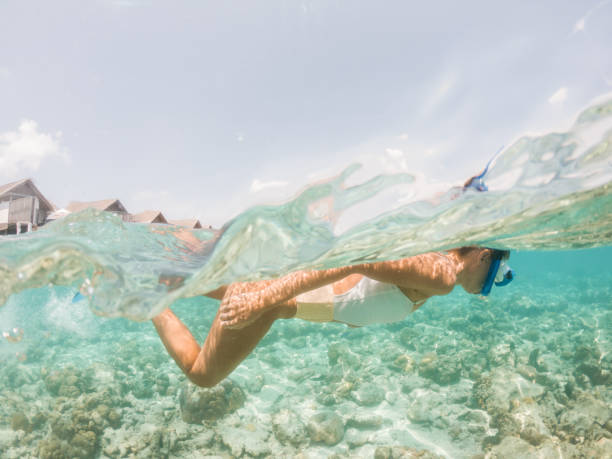 Woman dives in tropical sea, split screen underwater shot, overwater villas on background She explores the reef around the atoll in the Maldives, people on vacations, she adventures underwater vacation rental mask stock pictures, royalty-free photos & images