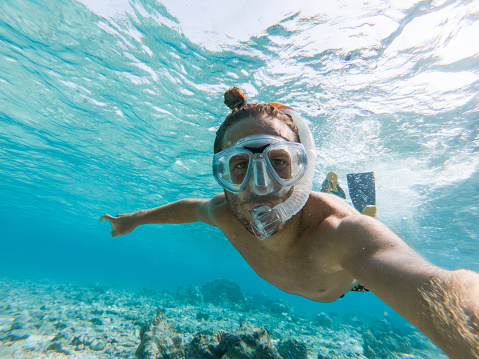 Female diver posing over hard coral reef with a school of anthias fish and other marine life. Scuba diving experience in Andaman sea, Thailand.