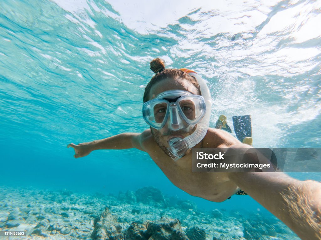 Young man takes selfie underwater with snorkelling mask He swims below the water surface and looks at the camera.
Man enjoying tropical vacations in the Maldives having fun exploring the underwater world Snorkeling Stock Photo