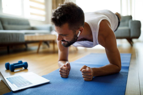 istock Young man with headphones using laptop for exercising at home 1311454562