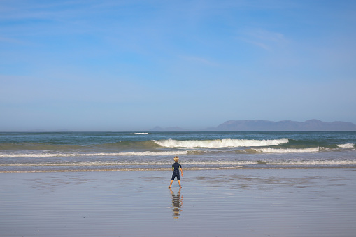 A young blond boy playing on the beach. He is alone watching the waves coming in.