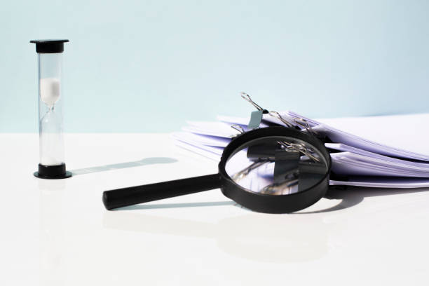 istock Scanning business documents. Magnifying glass on the stack of documents and an hourglass 1311457471