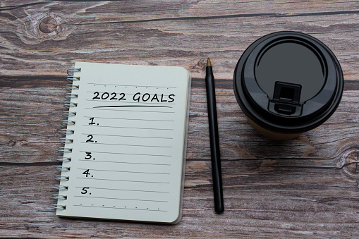 2022 goals text on notepad with a disposable coffee cup and pen on wooden desk