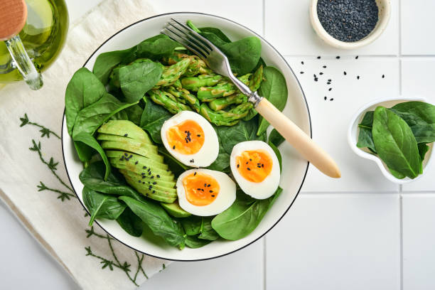 istock Fresh vegetable salad with avocado, asparagus, crumpled eggs with black sesame seeds and spinach on plate on light slate, stone or concrete background. Balanced lunch in bowl. Top view. Mock up. 1311461820