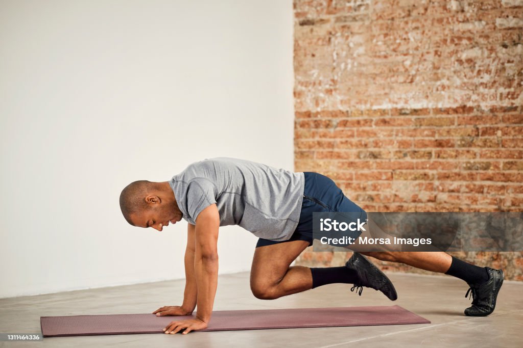 Sportsman Practicing Mountain Climbing Exercise Side view of sportsman practicing mountain climbing exercise. Male athlete is training at home. He is in sports clothing. Exercising Stock Photo