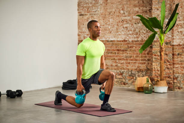 Male Athlete Doing Lunges With Kettlebells At Home Strong male athlete doing lunges with kettlebells. Sportsman is practicing in exercise room. He is in sports clothing at home. lunge stock pictures, royalty-free photos & images