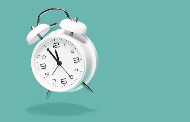 White bell alarm clock hovering over green background. 5 to 12 clock concept isolated. five to twelfe