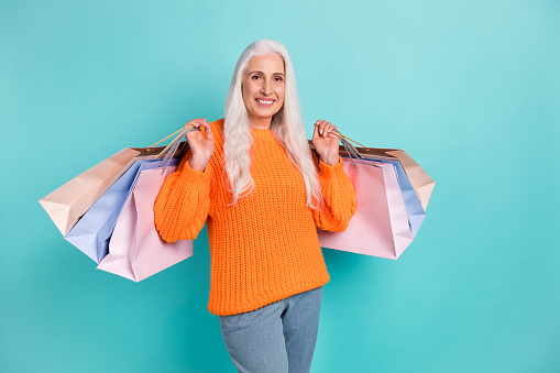 Photo of cheerful positive elderly woman hold hands shopping bags client black friday sale isolated on teal color background.