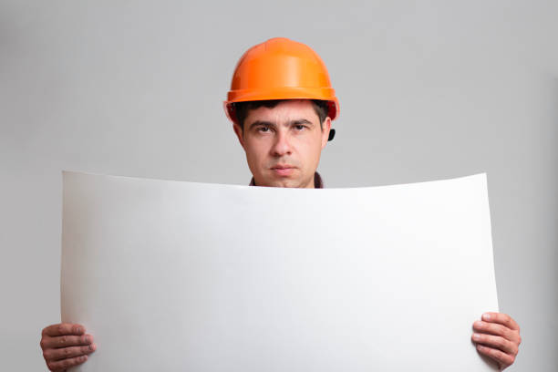 istock Young fatigue and angry construction worker in hard hat holding paper project on grey studio background 1311469072