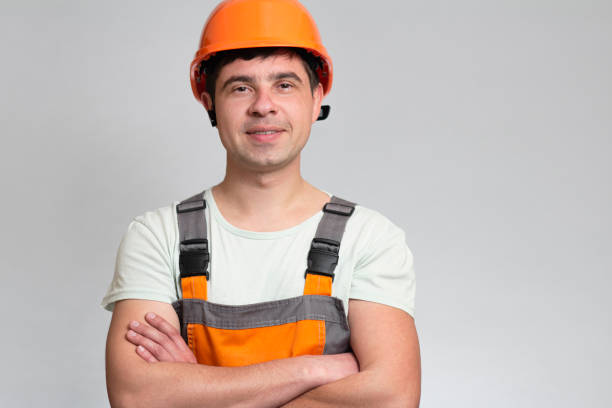 istock confident young construction worker in hard hat and overalls with arms folded on the chest on grey studio background 1311469237