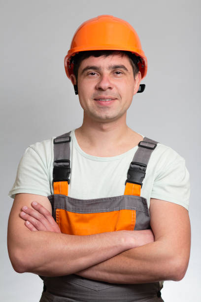 istock confident young construction worker in hard hat and overalls with arms folded on the chest on grey studio background 1311469274