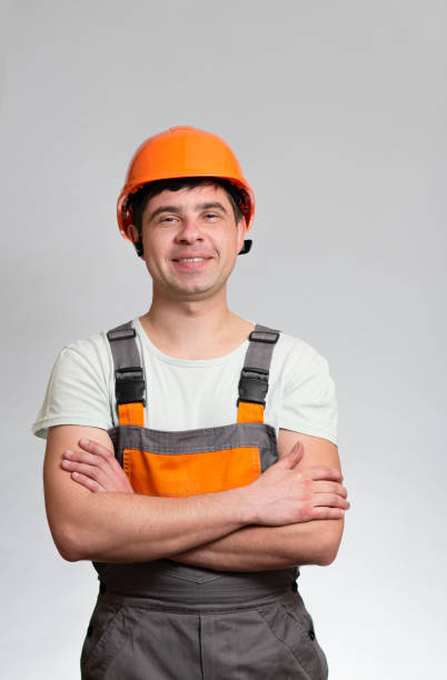istock confident young construction worker in hard hat and overalls with arms folded on the chest on grey studio background 1311469381