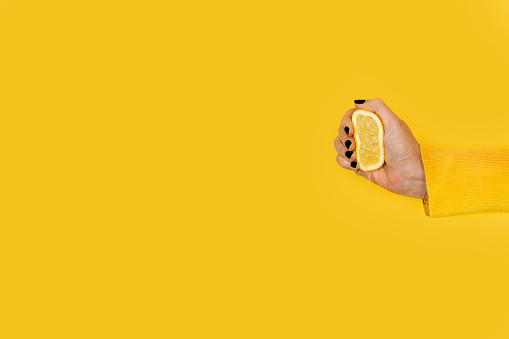 Woman squeezing a half lemon on a yellow background with copy space