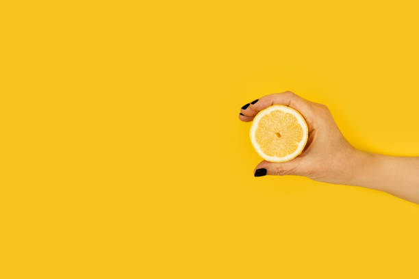 istock Woman hand holding a half lemon on a yellow background 1311470613