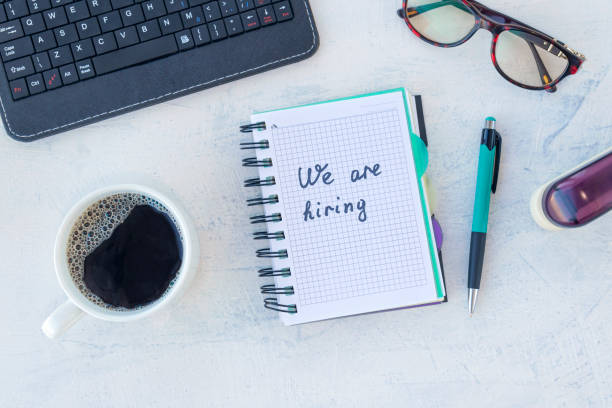 We are hiring. Job recruting concept. Words We are hiring in notebook on the working table. Top view stock photo