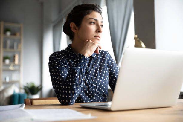 istock Thoughtful Indian female distracted from computer work looking into distance 1311475057