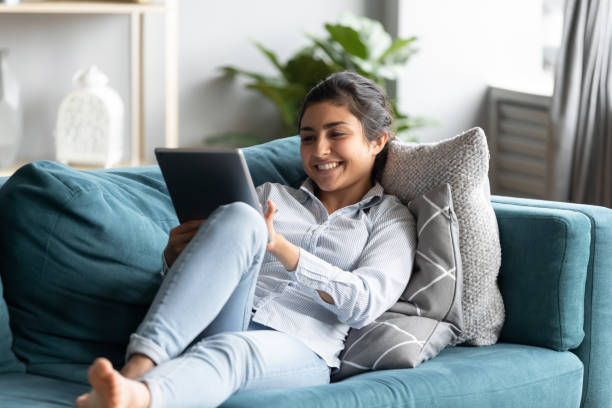 istock Relaxed indian girl lying on couch holding tablet enjoy e-shopping 1311475094